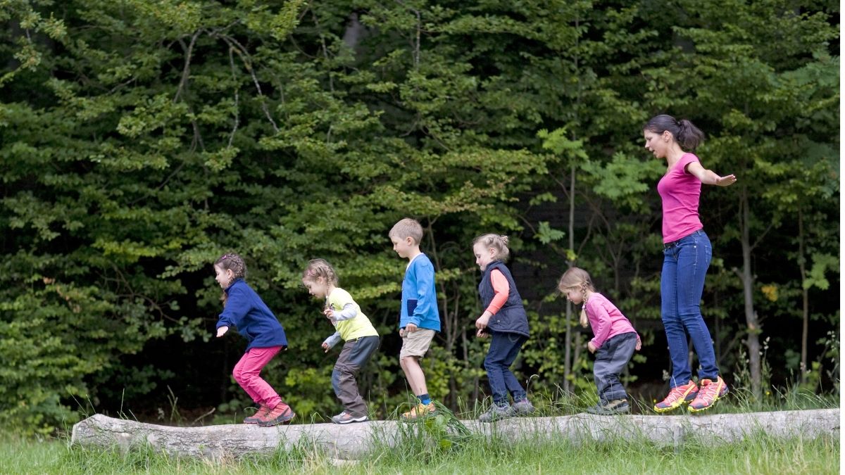 children and teacher balancing on log