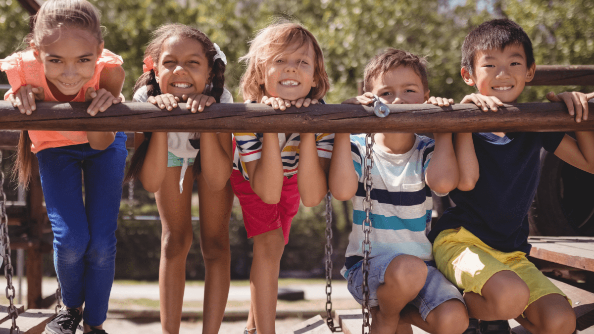 five children leaning on rail on wooden bridge at park