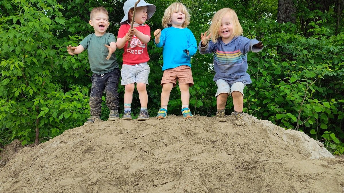 four young children standing in a row on a big rock