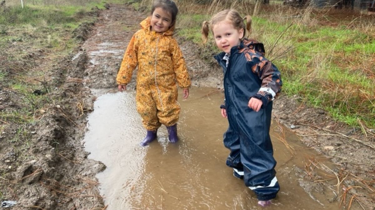 two children standing in a big rain puddle in rain gear