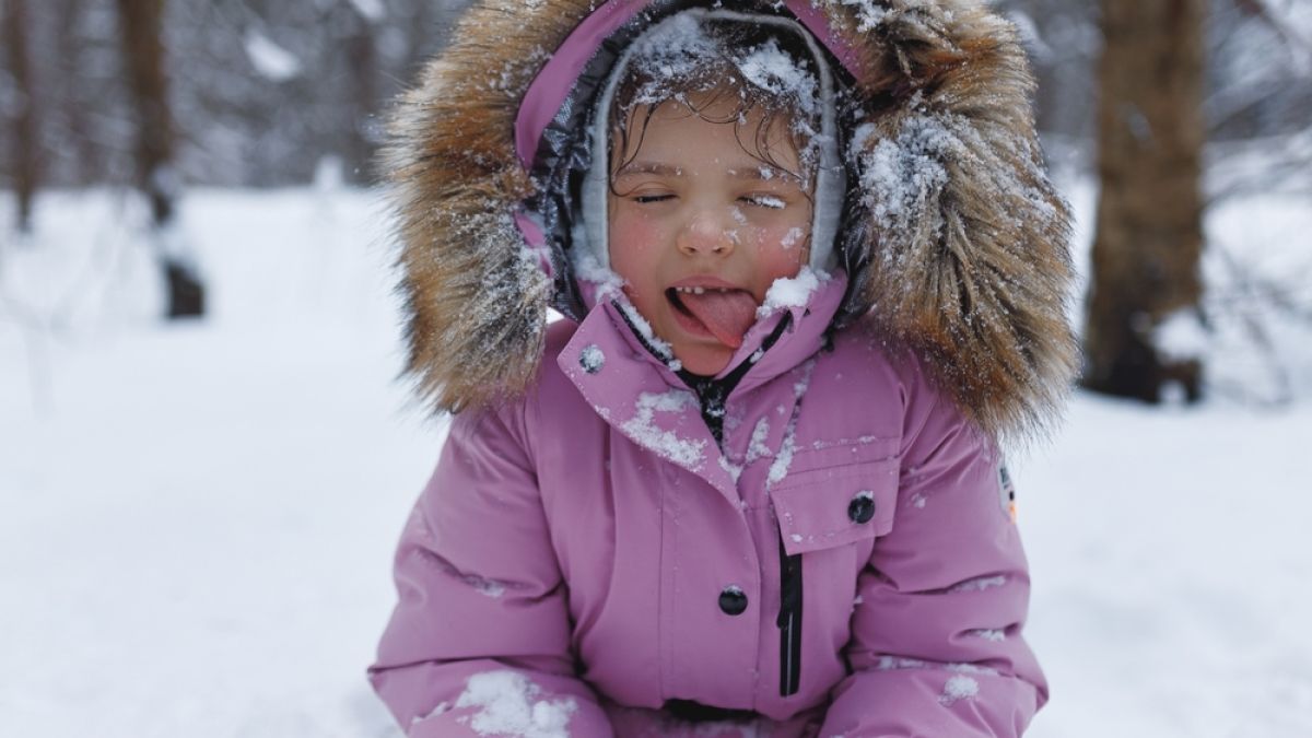 Child in pink snowsuit outside in snow, sticking out at camera