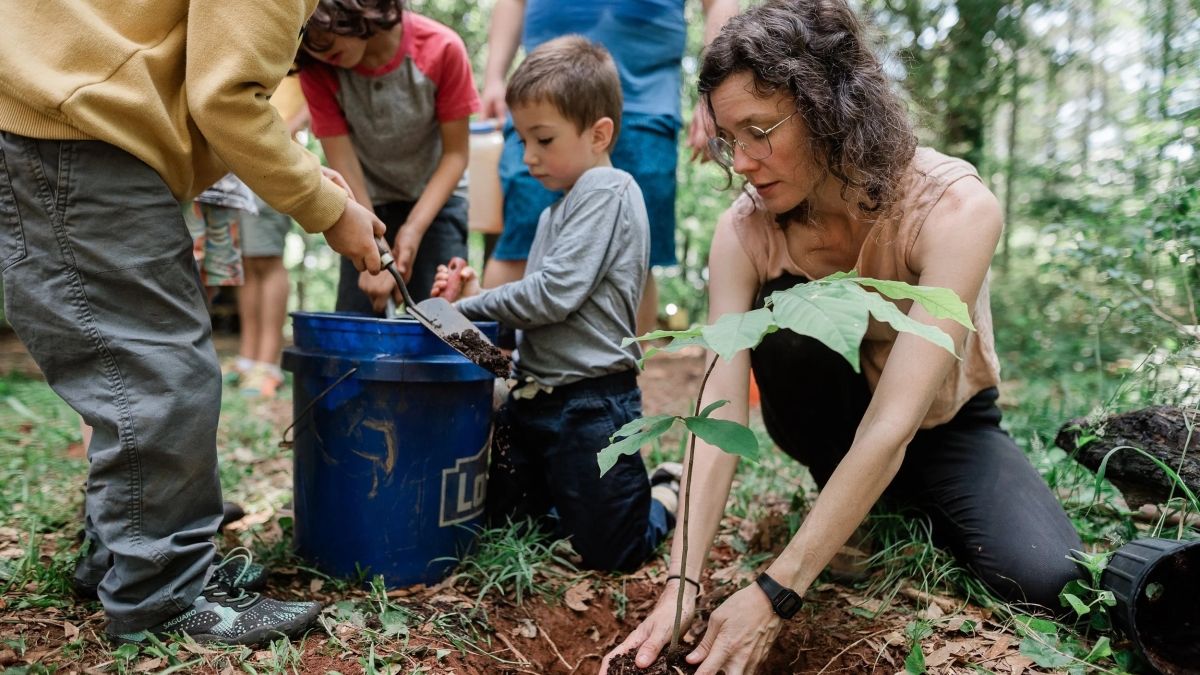 teacher and children planting a plant in the soil