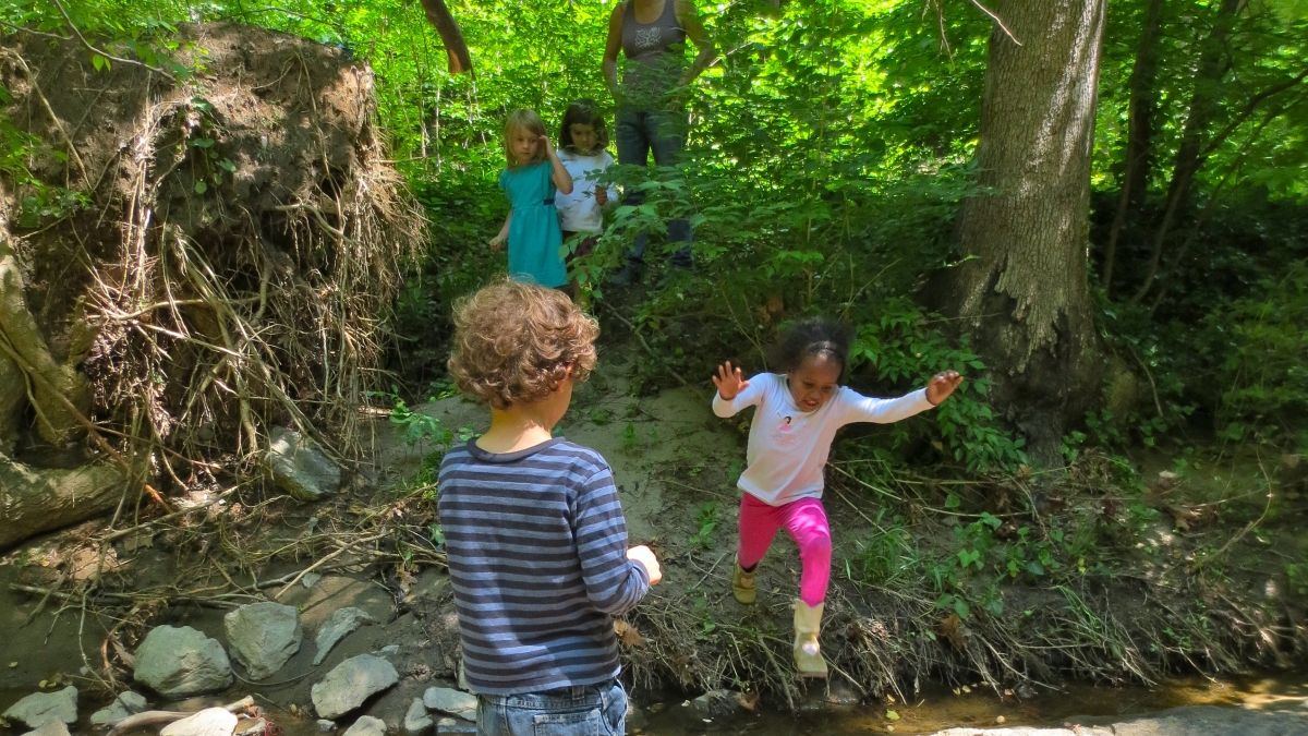 Children jump across the creek on a forest exploration.
