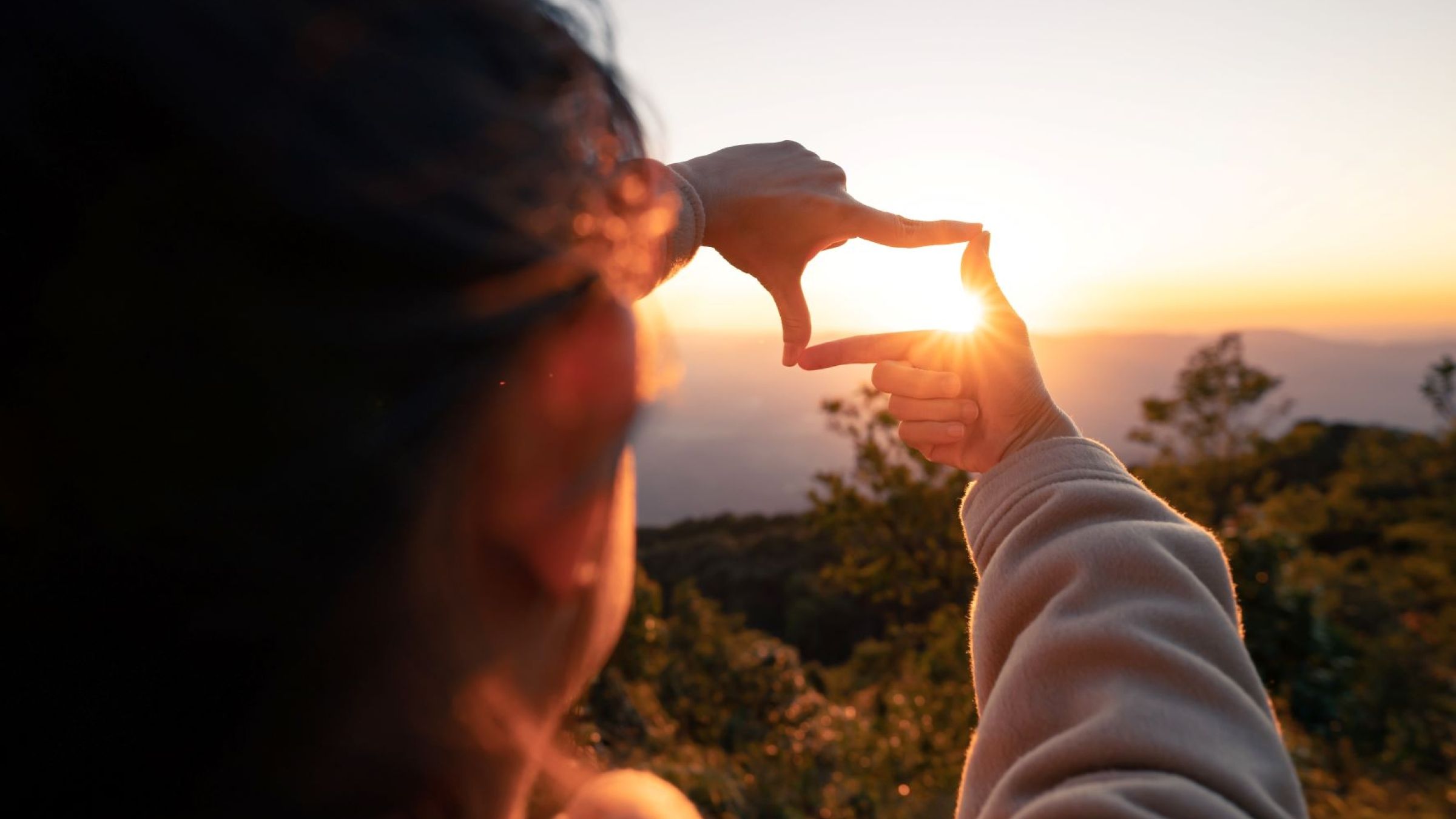 child forming frame around sunrise with fingers