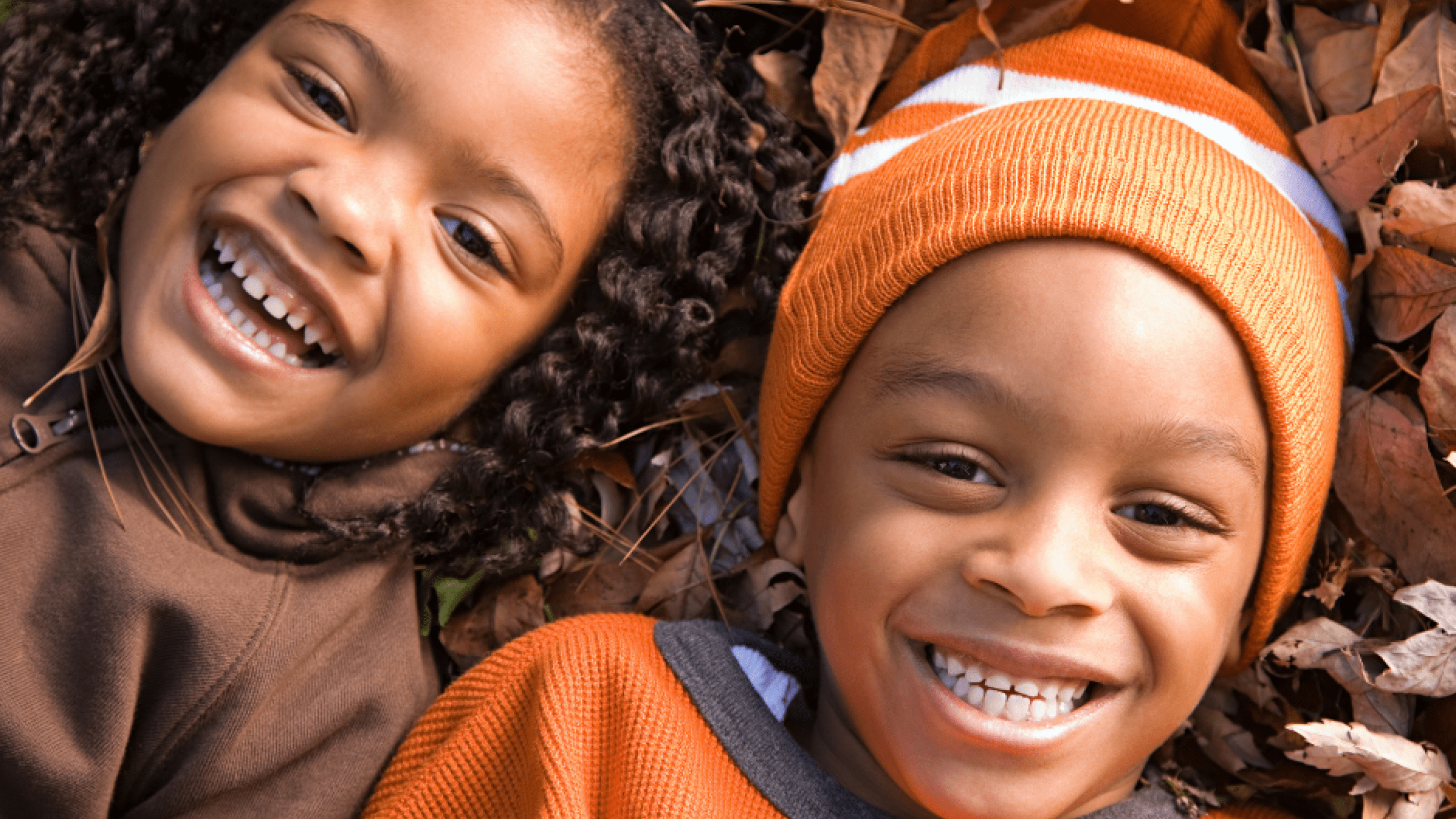 two smiling children laying on dry leaves