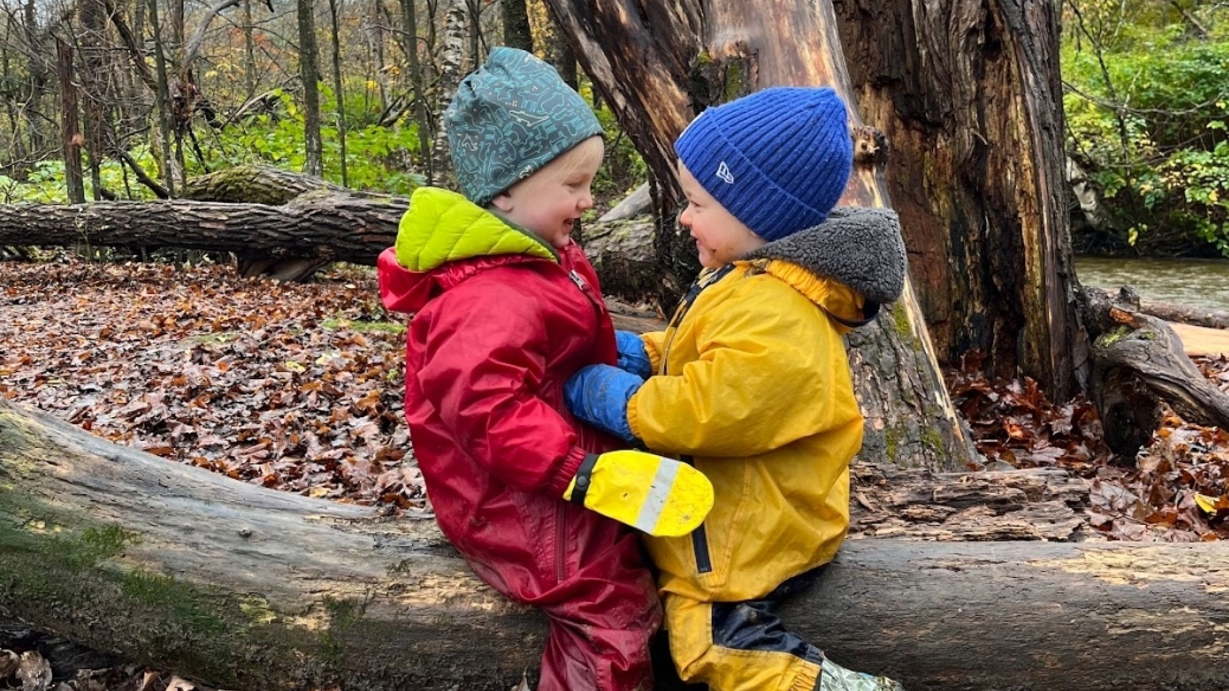 two children sitting on a log facing each other and laughing