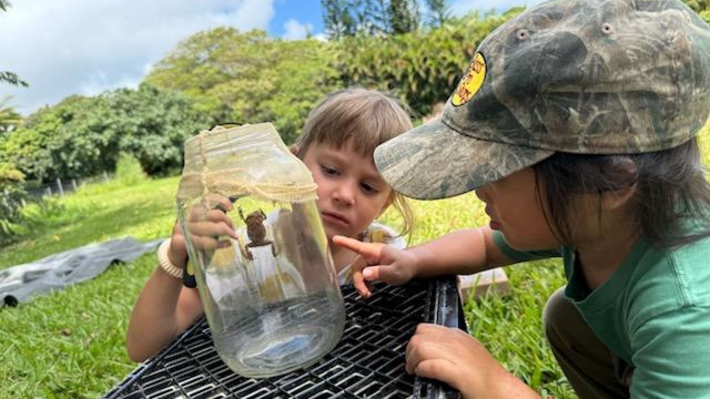 two children looking at a coqui frog in a jar