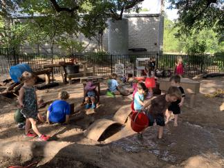 Young children playing in an outdoor sand and water area with a variety of loose parts.