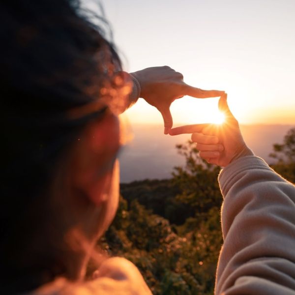 child forming frame around sunrise with fingers