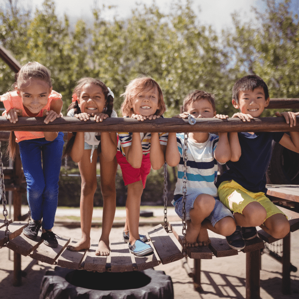 five children leaning on rail on wooden bridge at park