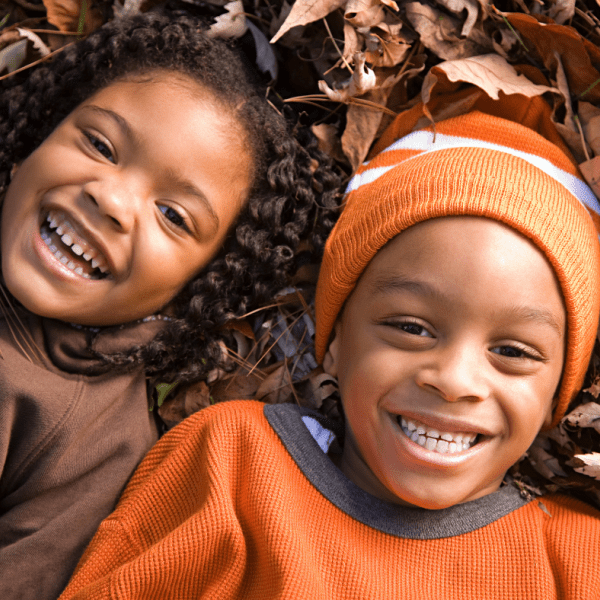 two smiling children laying on dry leaves
