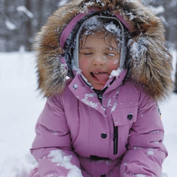 Child in pink snowsuit outside in snow, sticking out at camera