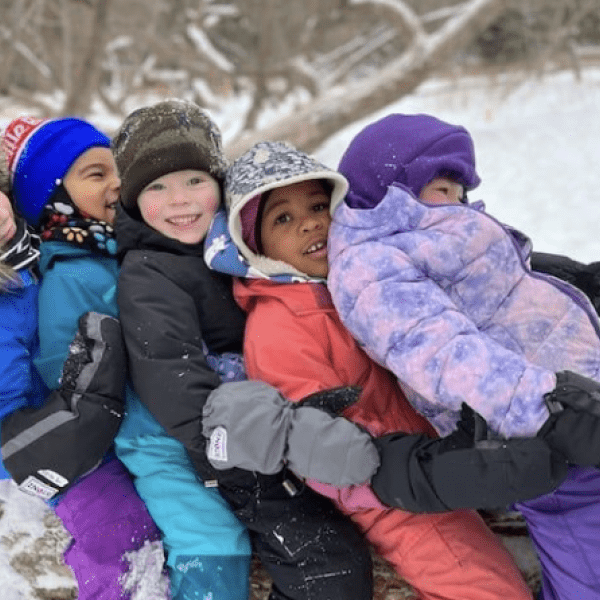 children sitting in a line on a tree branch in winter gear
